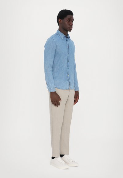Light blue denim button-up shirt, slim-fit beige trousers, and white sneakers. Features a classic collar and a subtle patterned detail.