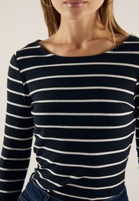 Langermet topp med marineblå og hvite horisontale striper, myk stoff, bred rund hals og glatt tekstur.
