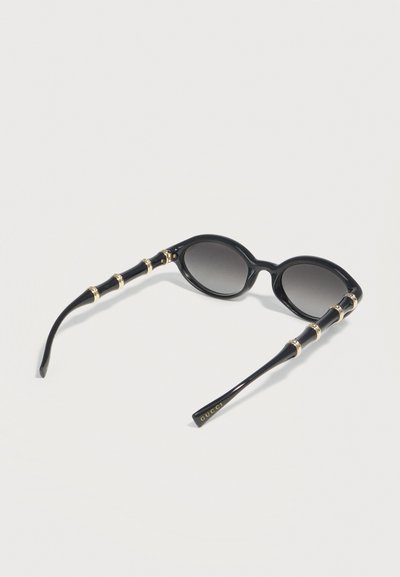Μαύρα οβάλ γυαλιά ηλίου με φακούς με διαβάθμιση και χρυσές λεπτομέρειες σε στυλ μπαμπού στα πλαϊνά, με το ένα πλαϊνό να φέρει το λογότυπο Gucci σε χρυσό.