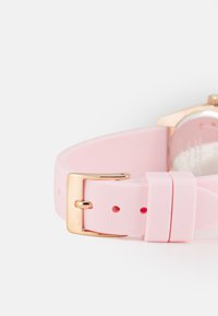 Bracelet de montre en silicone rose avec une boucle en métal doré et plusieurs trous pour l'ajustement. Texture lisse avec un design minimaliste.