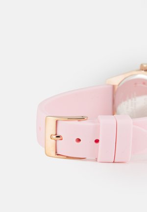 Cinturino per orologio in silicone rosa con una fibbia in metallo dorato e molteplici fori per la regolazione. Texture liscia con un design minimalista.