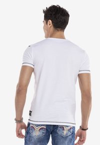 Weißes Baumwoll-T-Shirt mit kurzen Ärmeln, ausgestattet mit schwarzen Akzenten auf den Schultern und kontrastierendem Nähen an den Säumen und dem Saum.
