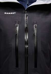 Μαύρο μπουφάν Mammut με τρεις κάθετους αδιάβροχους φερμουάρ και λευκή κουκούλα ορατή στην κορυφή.