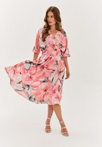 Kvetinové zavinovacie šaty v ružovej farbe s zelenými a modrými akcentmi. Vyrobené z ľahkého materiálu, s krátkymi rukávmi, opaskom v páse a vlniacou sukňou.