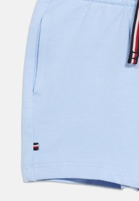 Υφασμα ανοιχτού μπλε χρώματος με πλαϊνή τσέπη και κορδόνι με ρίγες κόκκινου, λευκού και μαύρου, καθώς και μικρή ετικέτα κοντά στο τελείωμα.