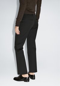 Zwarte op maat gemaakte broeken met een recht gesneden ontwerp, voorzien van twee achterzakken en een gladde textuur, gecombineerd met glanzende zwarte schoenen.
