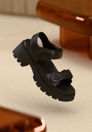 Sandali platform neri con due cinturini regolabili, una suola spessa e testurizzata, e dettagli con logo, che mostrano un design moderno e minimalista.