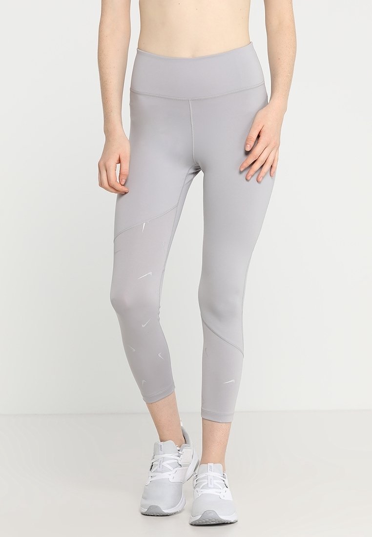Leggings de sport gris avec une taille haute, présentant une texture lisse et des motifs géométriques subtils. Associés à des baskets grises.