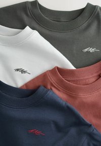 Četri džemperi tumši zilā, tumši zaļā, baltā un sarkankastanī. Katram ir ribota apkakle, un uz priekšpuses ir izšūta kontrastējoša logo.