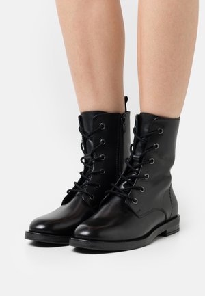 Bottines noires en cuir avec lacets, fermeture éclair latérale, bout rond, semelle plate et détails de couture subtils. La texture semble lisse et brillante.