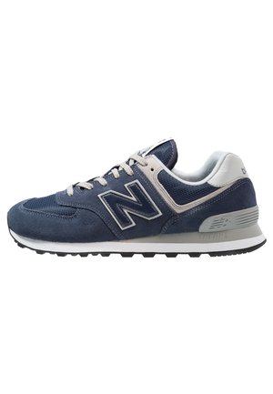Marineblå og grå New Balance sneaker med mesh og ruskind øverste, hvide snørebånd og sort gummisål vist fra siden.