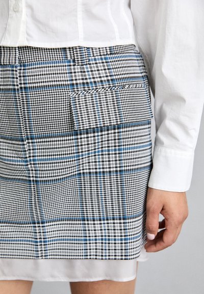 Plaid mini skirt featuring black, white, and blue patterns; structured fabric; includes a patch pocket on the back; paired with a white shirt.