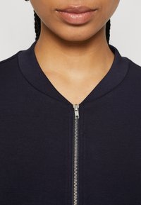 Close-up of a person wearing a navy blue zip-up garment with silver zipper, focusing on lips, chin, and neckline.