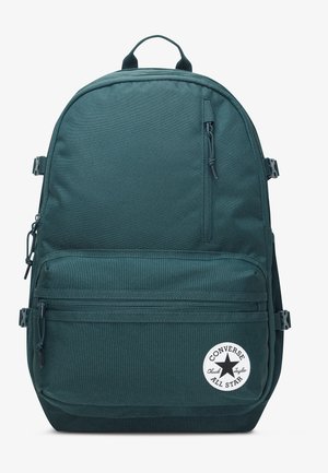 Ciemnozielony plecak Converse z przednimi i bocznymi kieszeniami na suwaki, regulowanymi paskami oraz okrągłą naszywką z logo Converse All Star na przedniej kieszeni.