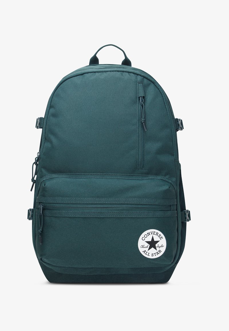 Sac à dos Converse vert foncé avec poches zippées à l'avant et sur les côtés, bretelles ajustables et un patch rond du logo Converse All Star sur la poche avant.