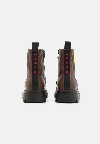 Stivali ankle in pelle marrone con suola in gomma nera, dotati di dettagli gialli, branding rosso sul retro e chiusura con zip.