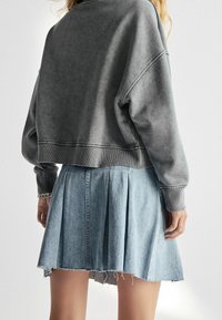 Grijze cropped sweatshirt met geribbelde manchetten, gecombineerd met een lichtblauwe denim plooirok met rafelige zoom en gestructureerde stof.