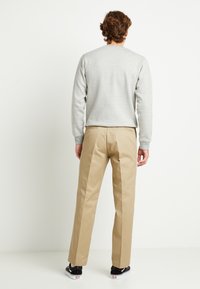 Šedý crewneck sweatshirt, khaki kalhoty a černé tenisky; hladká textura, volný střih, jednoduchý design bez viditelných vzorů nebo akcentů.