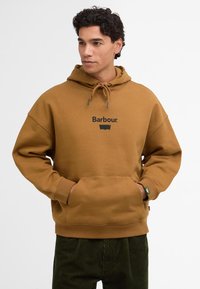 Καφέ φούτερ με κουκούλα και κορδόνι, μπροστινές τσέπες και μαύρο λογότυπο "Barbour". Συνδυάζεται με πράσινα τζιν καμπάνα. Χαλαρή, άνετη εφαρμογή.