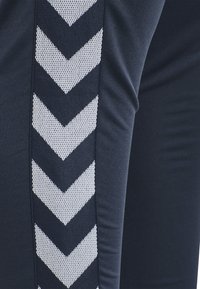 Marina atletiska leggings med ett texturerat silverfärgat chevronmönster längs sidan. Tillverkade av elastiskt, andningsbart material.