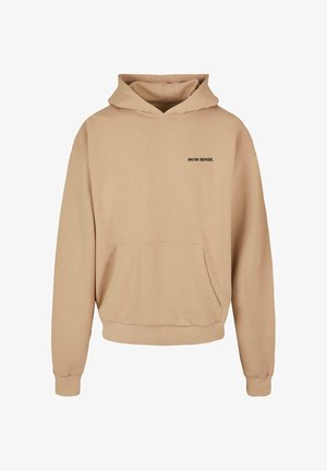 Bežs kapucis džemperis ar priekšējo kabatu, ribotām piedurknēm un melnu drukātu tekstu "9N1M SENSE." kreisajā krūšu zonā.