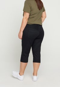 Mustat capri-housut, jotka on valmistettu denimistä ja joissa on tiukka muotoilu, kaksi takataskua ja sileä pinta, yhdistettyinä teksturoituun oliivinvihreään puseroon.