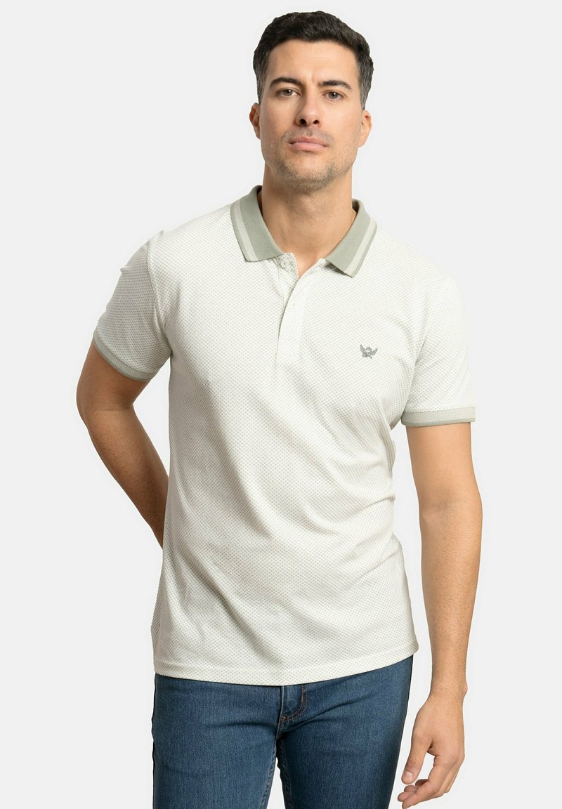 Camisa polo blanca con un patrón texturizado, con cuello y puños de color verde claro, logo bordado en el pecho, combinada con jeans de mezclilla azul.