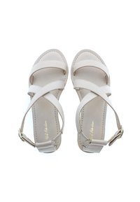 Beiga lädersandaler med korsremmar, en platt sula och ett ankelband med en gyllene spänne. Slät textur med sömdetaljer.