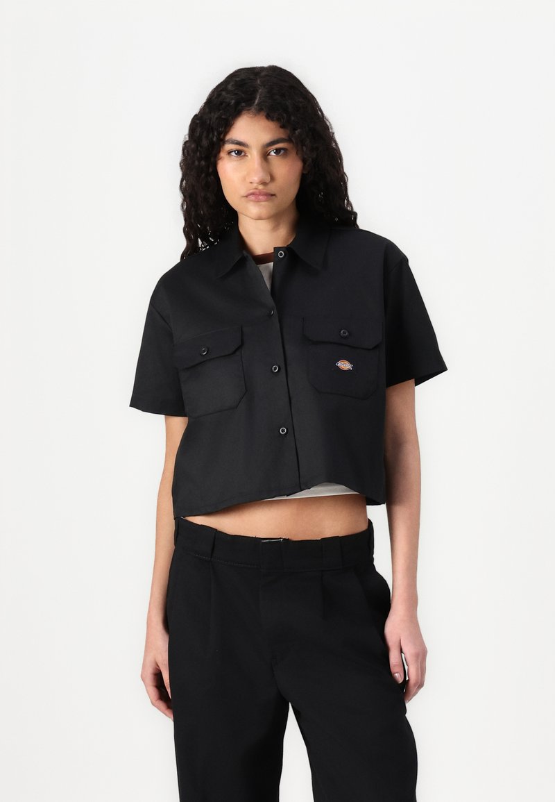 Camiseta cropped preta feita de tecido leve; apresenta mangas curtas, dois bolsos no peito e um pequeno detalhe de logotipo no bolso esquerdo.