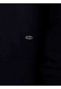 Maglione blu navy con orlo a coste e una piccola etichetta in metallo argentato. Il tessuto sembra a maglia con una superficie liscia.