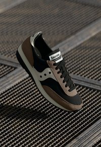 Black and brown Saucony sneaker with white sole and logo, positioned on a textured metal surface.