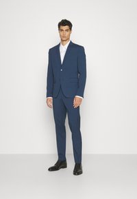 Navy blue suit comprising a tailored jacket with a single button and notch lapels, paired with slim-fit trousers and black dress shoes.