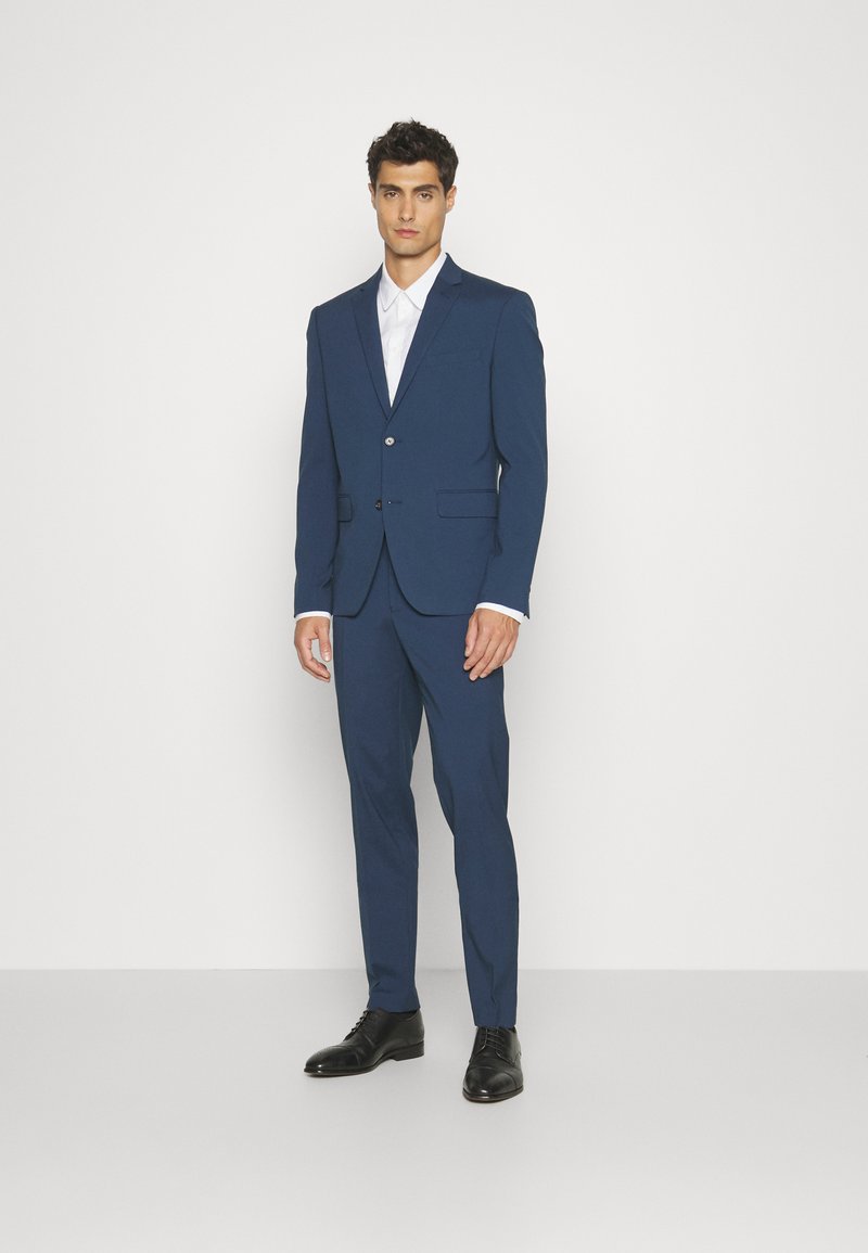 Navy blue suit comprising a tailored jacket with a single button and notch lapels, paired with slim-fit trousers and black dress shoes.