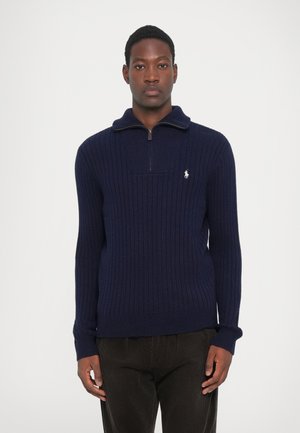 Pull en tricot côtelé bleu marine avec un col zippé et un petit logo sur la poitrine. Présente des manches longues et une coupe structurée.