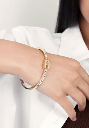 Gold-tone bangle bracelet featuring clear rhinestones, a smooth surface, and a distinctive lock shape accent. Worn on a wrist.