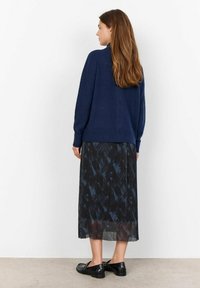 Maglione a maglia blu navy abbinato a una gonna nera plissè con un motivo astratto scuro. Il modello indossa scarpe basse nere.