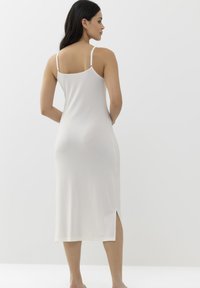 Robe à fines bretelles blanche sans manches en tissu doux, mi-longue avec une fente sur le côté, bretelles ajustables et silhouette ajustée.