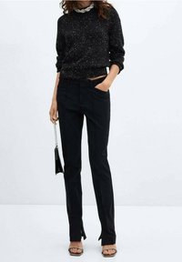 Czarny, dzianinowy sweter z plamkowanym wzorem. Dopasowane czarne spodnie z bocznymi rozcięciami na dole. Dodatki to mała czarna torebka.