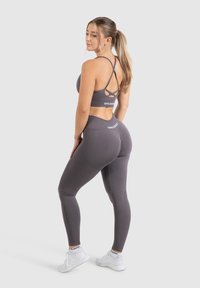 Grijze sportset met een crisscross rug sportsbra en high-waisted legging met gestructureerde accenten. Witte logo-detail op beide stukken.