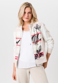 Lichte zip-up jas in roomwit met rode en zwarte bloemenprints. Bevat een hoge kraag en contrasterende stofpanelen.