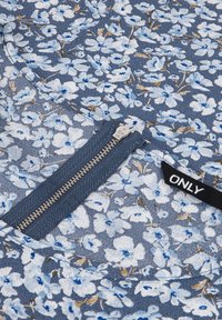 Abito a fantasia floreale in tonalità blu con fiori bianchi e beige. Presenta una zip centrale e un'etichetta del marchio, realizzato in tessuto morbido.