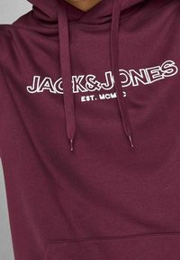 Sudadera con capucha burdeos con logo blanco "JACK&JONES EST. MCMXC", capucha con cordón y bolsillo delantero. Tejido suave con textura lisa.