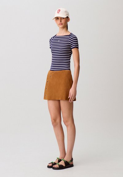 Top a righe navy e bianco a maniche corte con costine abbinato a una minigonna in suede color cammello con dettagli a bottoni. Sandali neri con dettagli verdi.