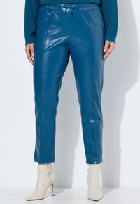Blå konstläderbyxor med slim fit, elastisk midja och dragsko. Ankellånga, kombinerade med krämfärgade högklackade stövlar.