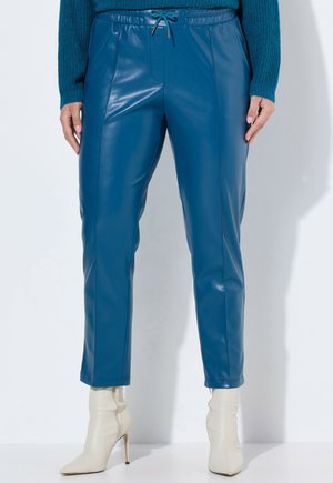 Pantalons en simili cuir bleu avec une coupe ajustée, une taille élastique et un cordon de serrage. Longueur cheville, associés à des bottes à talons hauts de couleur crème.