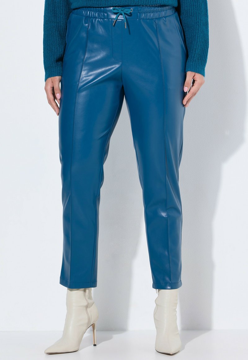 Blå konstläderbyxor med slim fit, elastisk midja och dragsko. Ankellånga, kombinerade med krämfärgade högklackade stövlar.