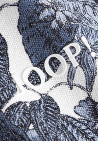 Bomullstyg med ett blått blommönster på vit bakgrund, med en framträdande vit präglad logotyp "JOOP!" i förgrunden.