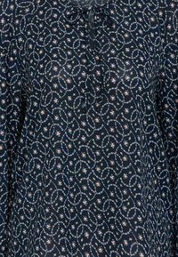 Blusa floreale scura con scollo a fiocco. Presenta un motivo vorticoso di piccoli fiori e vigneti in colori pastello su uno sfondo blu navy.