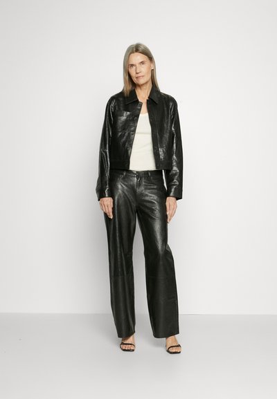 Black leather cropped jacket and high-waisted trousers, smooth texture, minimal design, paired with black strappy sandals, neutral top.