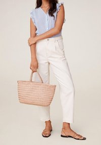 Pantaloni bianchi a vita alta, blusa a righe blu chiaro con maniche a volant e borsa rosa intrecciata. La modella indossa sandali con lacci.